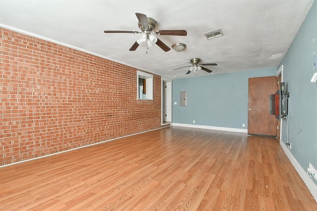 empty room with wood finished floors, visible vents, brick wall, and baseboards