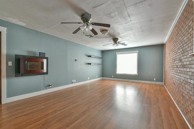 empty room with visible vents, brick wall, a textured ceiling, and wood finished floors