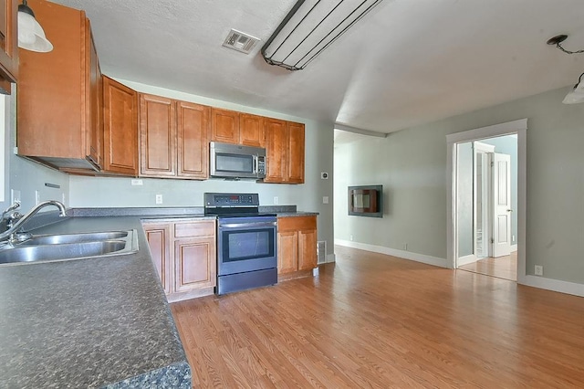 kitchen featuring visible vents, light wood-style flooring, appliances with stainless steel finishes, brown cabinetry, and a sink