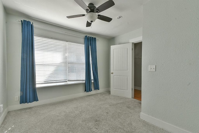 carpeted spare room with a ceiling fan, baseboards, and a textured wall