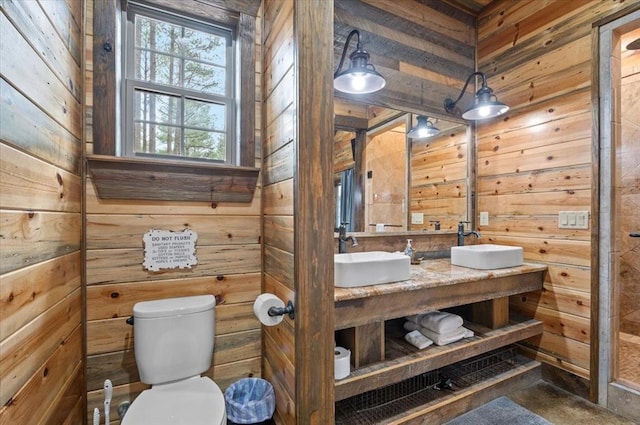 bathroom with double vanity, toilet, wood walls, and a sink