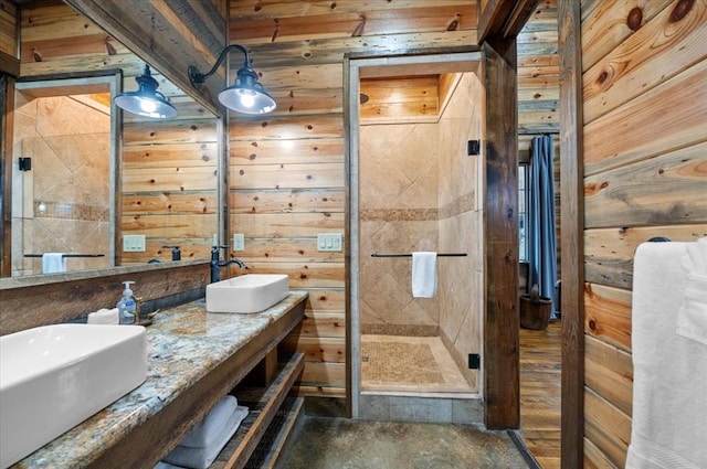 bathroom with double vanity, a stall shower, wood walls, and a sink