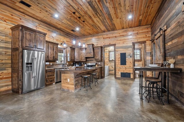 kitchen featuring a kitchen breakfast bar, a center island, appliances with stainless steel finishes, wooden ceiling, and concrete flooring