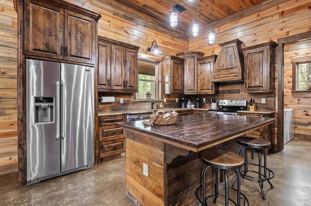 kitchen featuring custom range hood, finished concrete floors, wooden walls, appliances with stainless steel finishes, and wooden counters