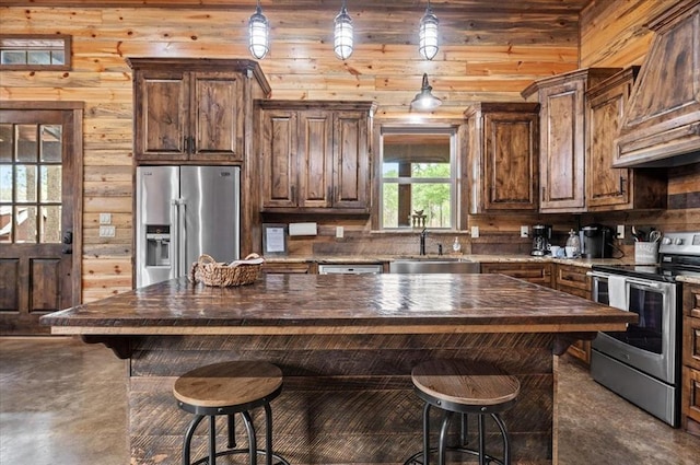 kitchen with premium range hood, butcher block countertops, hanging light fixtures, stainless steel appliances, and a sink