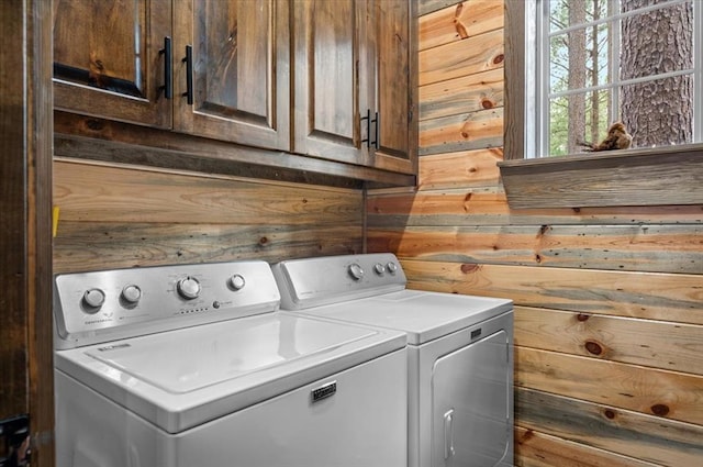 washroom featuring washer and dryer, wooden walls, and cabinet space