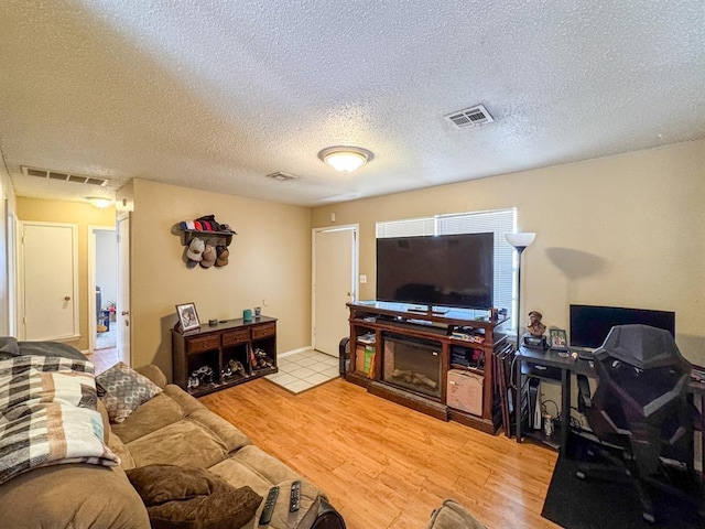 living room featuring visible vents, light wood finished floors, and a textured ceiling