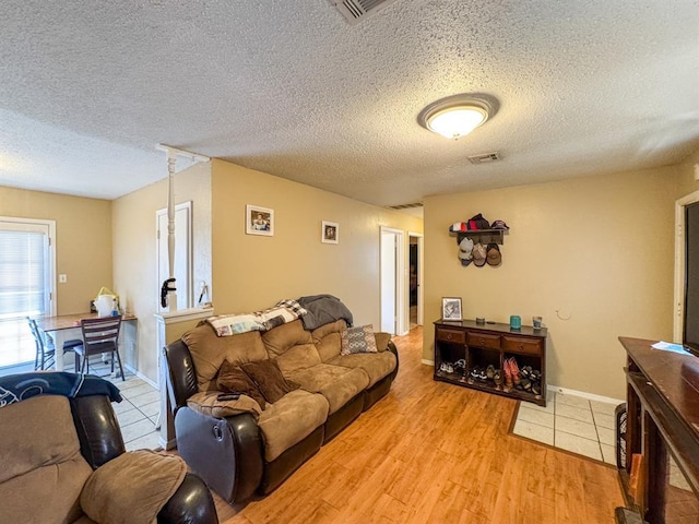 living room with visible vents, baseboards, light wood-style floors, and a textured ceiling