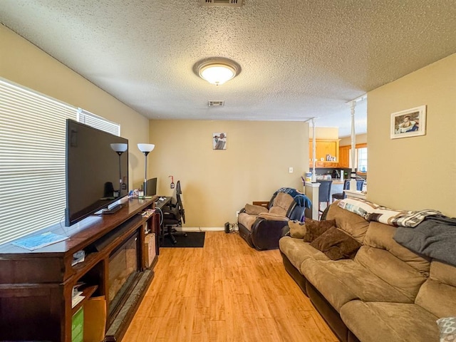 living area with visible vents, baseboards, a textured ceiling, and light wood-style flooring