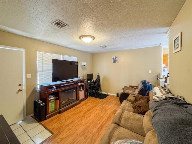 living room featuring a textured ceiling, baseboards, visible vents, and light wood-type flooring