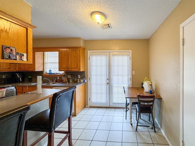 kitchen with light tile patterned floors, brown cabinetry, visible vents, and a textured ceiling