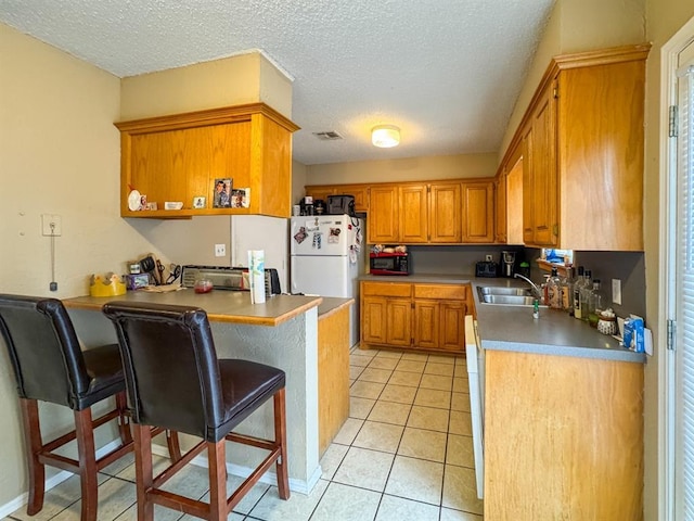 kitchen with light tile patterned floors, brown cabinetry, a peninsula, freestanding refrigerator, and a textured ceiling