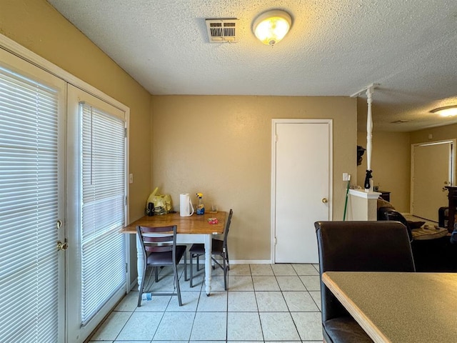 dining space with light tile patterned flooring, visible vents, a textured ceiling, and baseboards