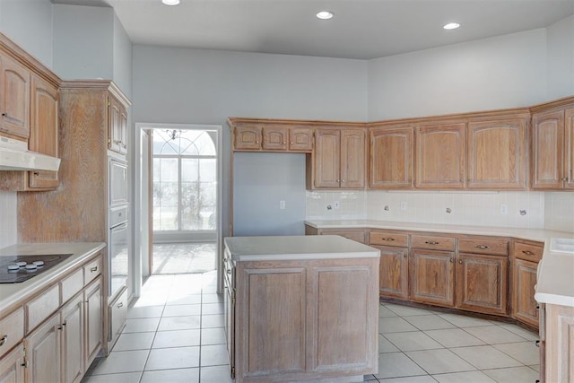 kitchen featuring decorative backsplash, under cabinet range hood, a kitchen island, light tile patterned floors, and black electric cooktop