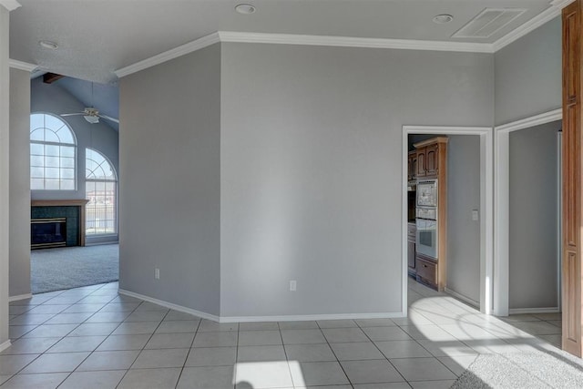 spare room featuring visible vents, ornamental molding, light tile patterned floors, a glass covered fireplace, and a ceiling fan