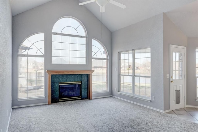 unfurnished living room featuring baseboards, carpet floors, a tile fireplace, high vaulted ceiling, and a ceiling fan