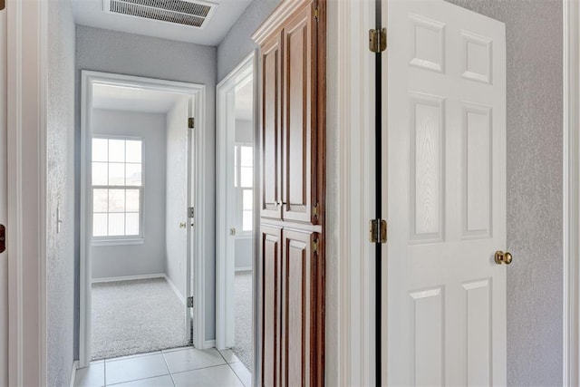 hall with light tile patterned floors, visible vents, baseboards, and light colored carpet