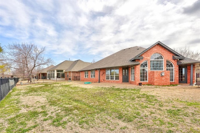 back of property with brick siding, a lawn, roof with shingles, and fence