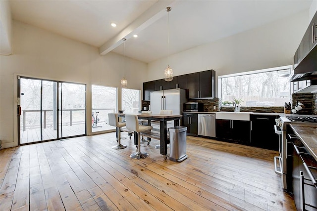 kitchen with beam ceiling, tasteful backsplash, a high ceiling, light wood-style floors, and appliances with stainless steel finishes