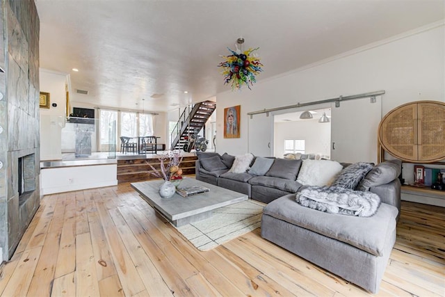 living area with wood-type flooring, ornamental molding, stairs, and a tiled fireplace