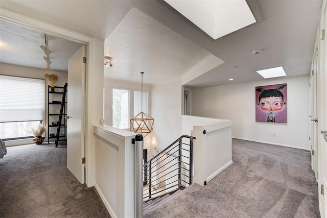 hall with an upstairs landing, baseboards, a skylight, and carpet