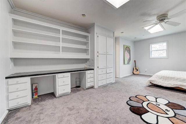 bedroom featuring built in desk, light colored carpet, a skylight, and baseboards