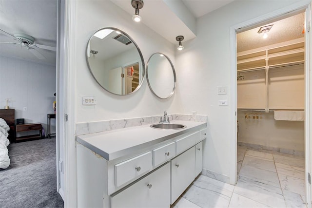 bathroom with marble finish floor, vanity, baseboards, ceiling fan, and a spacious closet