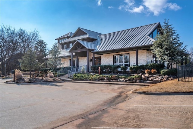 view of front facade with stone siding, metal roof, a standing seam roof, and fence