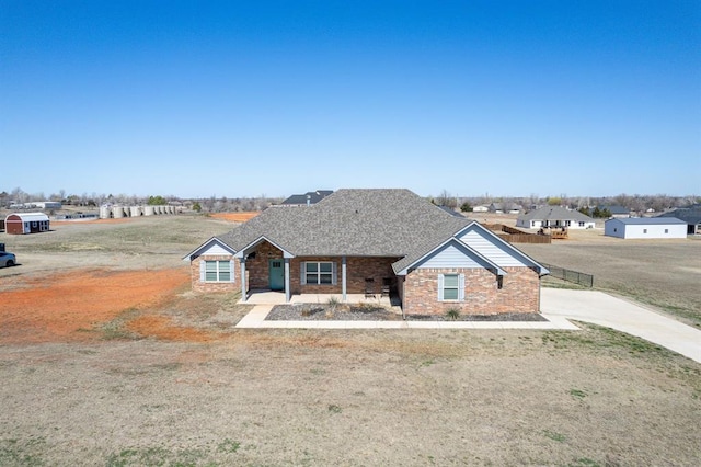 view of front of house featuring brick siding, roof with shingles, and fence