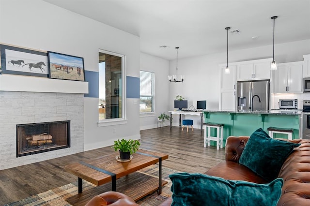 living area with wood finished floors, baseboards, visible vents, a stone fireplace, and a chandelier