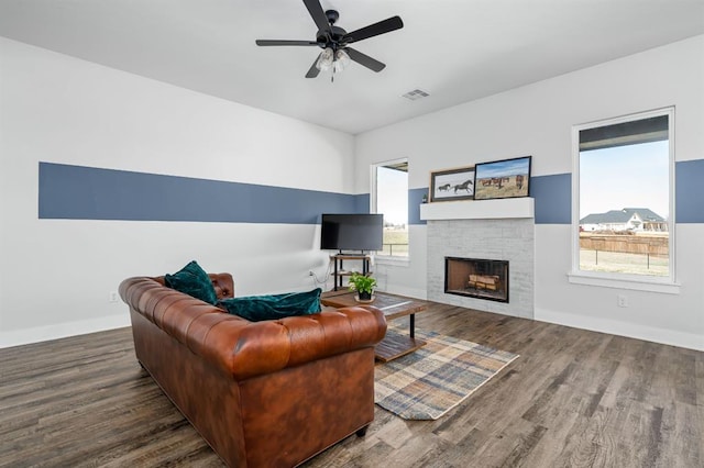 living area featuring visible vents, a stone fireplace, baseboards, and wood finished floors