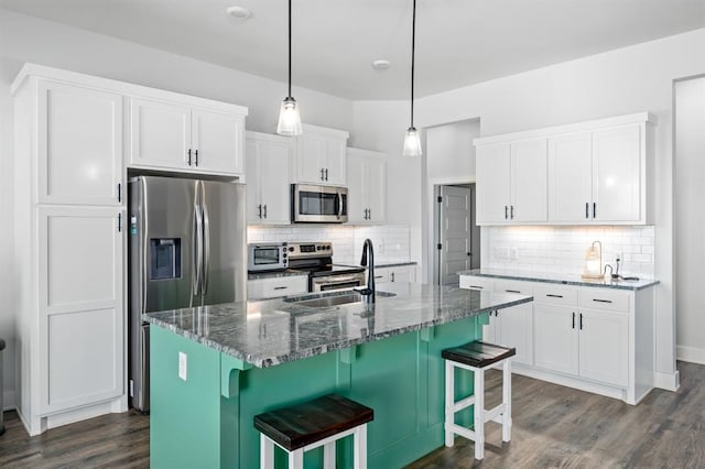 kitchen with a sink, dark wood-style floors, stainless steel appliances, dark stone counters, and white cabinets