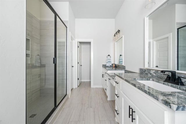 full bath featuring a sink, baseboards, two vanities, and a shower stall