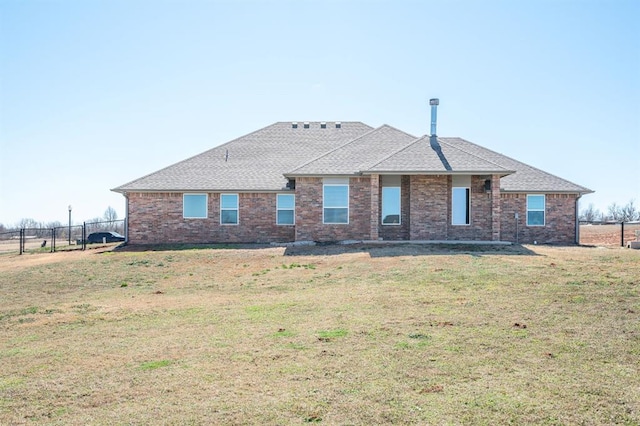 back of property featuring brick siding, fence, a lawn, and a shingled roof