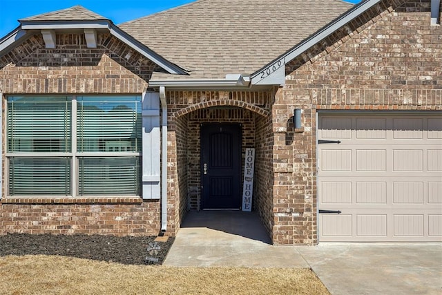 doorway to property featuring a garage, brick siding, and a shingled roof