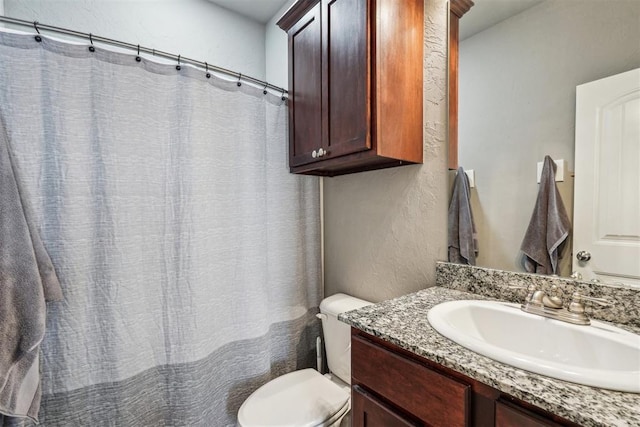 full bathroom featuring toilet, vanity, and a textured wall