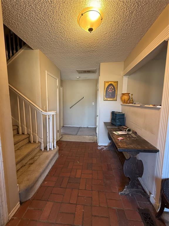 hallway with visible vents, stairway, a textured ceiling, and brick floor