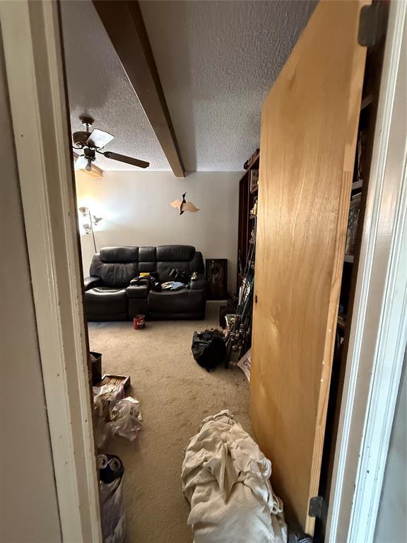 interior space with beam ceiling, a textured ceiling, and a ceiling fan