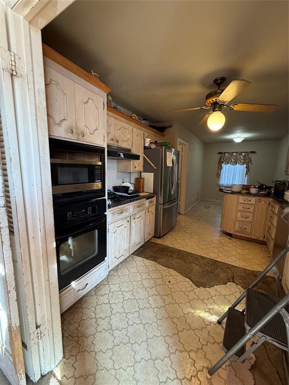 kitchen featuring black appliances, stone finish floor, under cabinet range hood, dark countertops, and ceiling fan