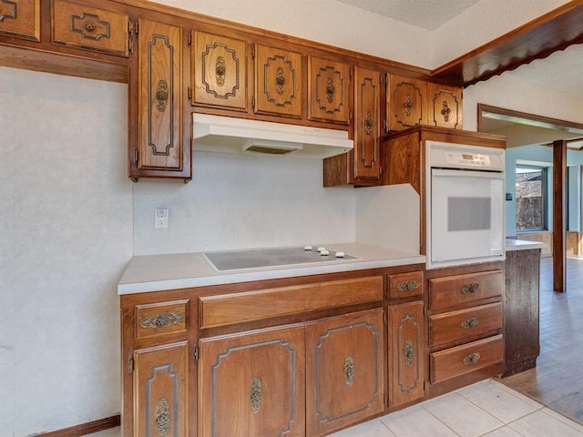 kitchen with electric stovetop, brown cabinets, under cabinet range hood, and oven