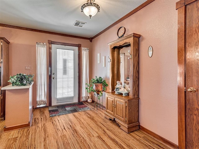 foyer entrance with visible vents, ornamental molding, light wood-style floors, baseboards, and a textured wall