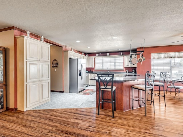 kitchen with a breakfast bar, stainless steel refrigerator with ice dispenser, dark countertops, white cabinetry, and light wood finished floors