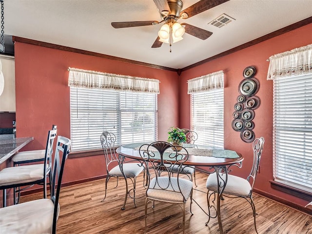 dining area featuring wood finished floors, baseboards, visible vents, ceiling fan, and crown molding