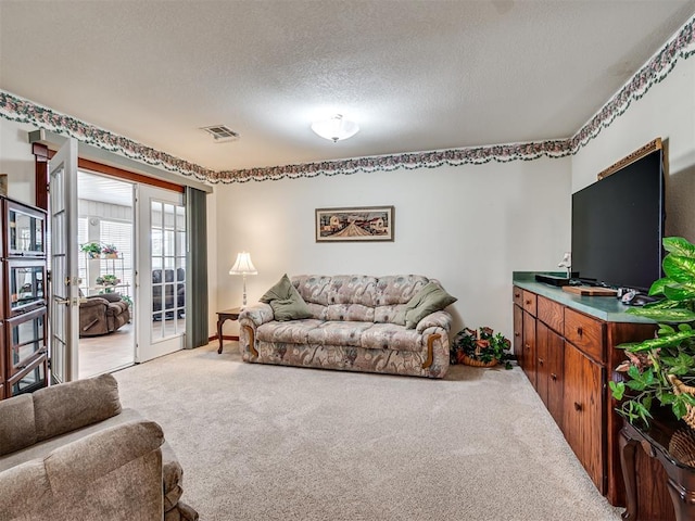 living area with visible vents, light colored carpet, and a textured ceiling