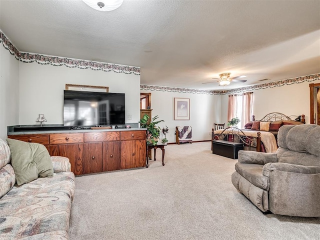 living area with a ceiling fan, light colored carpet, baseboards, and a textured ceiling