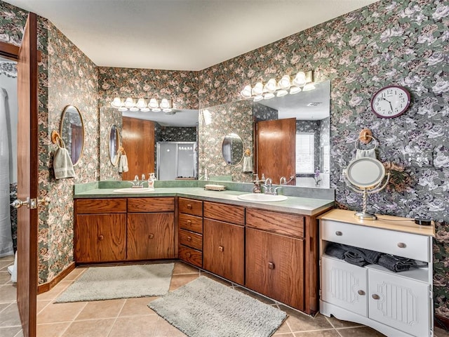 full bath with double vanity, tile patterned floors, wallpapered walls, and a sink