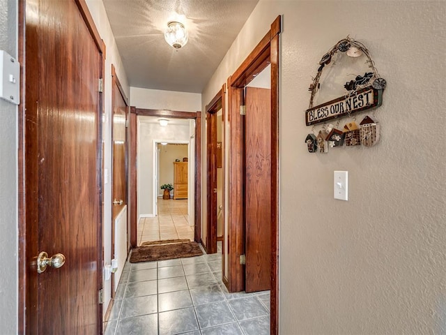 hall featuring tile patterned flooring, a textured ceiling, and a textured wall