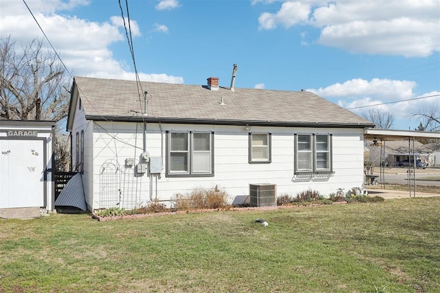 back of house with a carport, central air condition unit, a yard, and a shingled roof