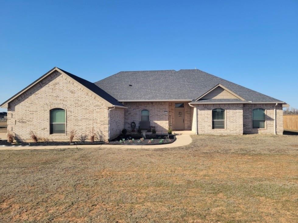 view of front of house featuring brick siding, roof with shingles, and a front yard