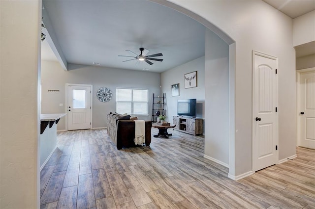 living room featuring baseboards, visible vents, arched walkways, ceiling fan, and light wood-style floors
